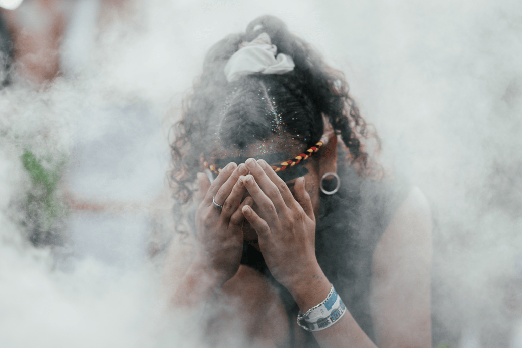 An Aboriginal woman in covers her face and crouches down in healing smoke.